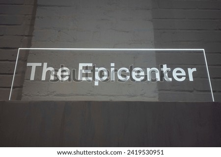 Low angle view of edge lit acrylic signage, "The Epicenter," isolated against white brick wall background.