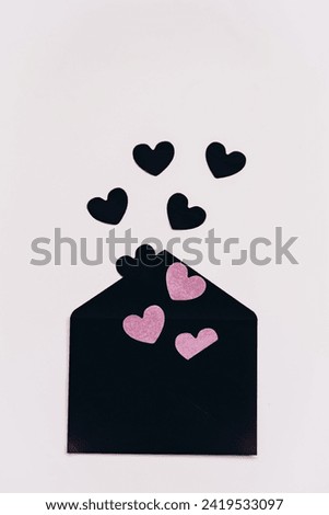 black envelope with black and pink paper hearts on a light background. preparation for Valentine's Day. a gift for Valentine's Day. an invitation to love