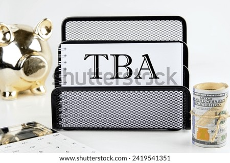 TBA text on a white piece of paper next to a piggy bank, a roll of money and a calculator on a white background