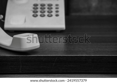 close up black and white photo of a telephone receiver on a hotel table.