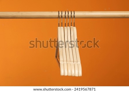 Empty clothes hangers on wooden rack against orange background