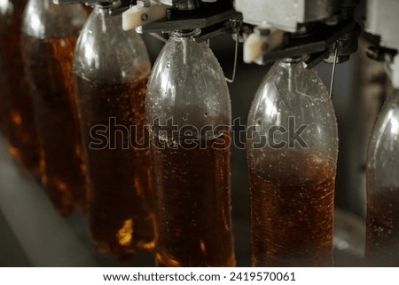Several plastic bottles hanging on belt conveyor or assembly line during process of filling soda or lemonade before packaging Royalty-Free Stock Photo #2419570061
