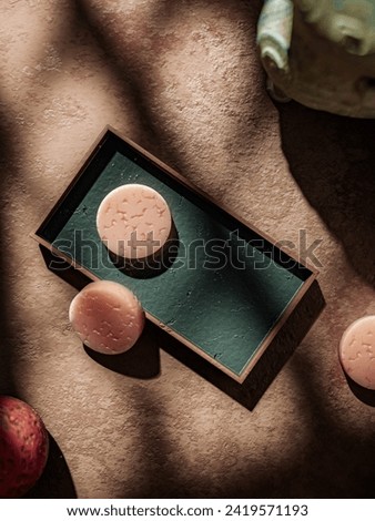Soothing indulgence: Cozy spa corner, warm grid-lit vibe. Green tray, pink handmade soap. Ideal for product placement, blending luxury and tranquility in a visual symphony. Royalty-Free Stock Photo #2419571193