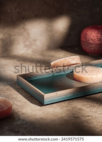 Soothing indulgence: Cozy spa corner, warm grid-lit vibe. Green tray, pink handmade soap. Ideal for product placement, blending luxury and tranquility in a visual symphony. Royalty-Free Stock Photo #2419571575
