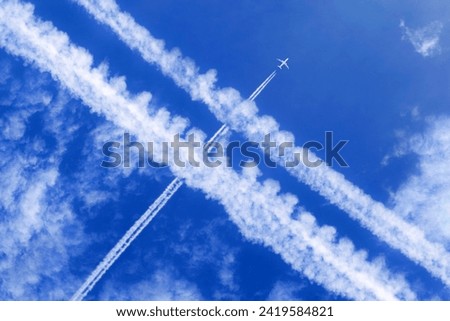 a passenger aircraft with contrails in the blue sky crosses other contrails Royalty-Free Stock Photo #2419584821
