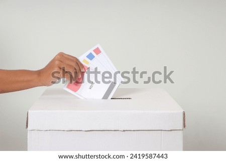 Close up of hand inserting and putting the voting paper into the ballot box. General elections or Pemilu for the president and government of Indonesia. Isolated image on white background Royalty-Free Stock Photo #2419587443