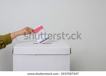Close up of hand inserting and putting the voting paper into the ballot box. General elections or Pemilu for the president and government of Indonesia. Isolated image on white background
