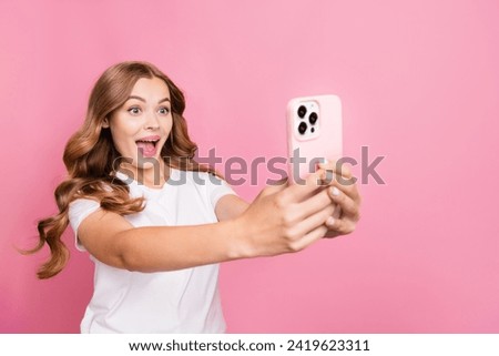 Photo of overjoyed woman with wavy hairstyle dressed white t-shirt making awesome pictures on smartphone isolated on pink color background