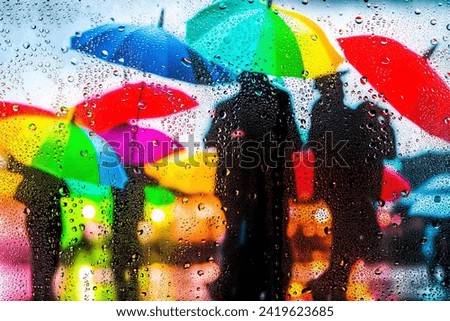 View through glass covered with raindropson as teenagers playing in the rain  a city square hung with a large number of colorful umbrellas, rainy mood.focus and sharpness on raindrops