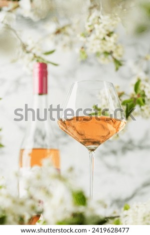 Rose wine glass against white wall with spring cherry flowers. Refreshing alcoholic summer drink or nature concept.