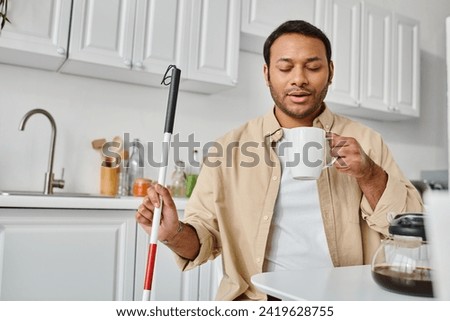 attractive indian man with visual impairment sitting and drinking tasty coffee while on kitchen Royalty-Free Stock Photo #2419628755