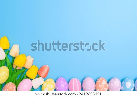 Happy Easter holiday greeting card concept. Colorful Easter Eggs and spring flowers on blue background. Top view, flat lay, copy space.