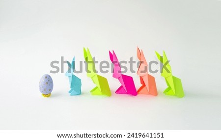 Multi-colored Easter bunnies made of paper, origami on a light background.  Easter holiday concept, race for Easter eggs.  Front view, background image.