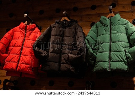 Down jacket for adults. Stylish, green, red, black warm winter jacket for adults on the shop window. Winter fashion