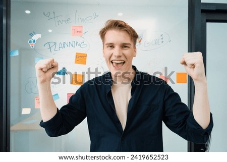 Portrait of happy young businessman wearing blue casual uniform while standing in front of glass board with colorful sticky notes and mind map with confident at creative business meeting. Immaculate.