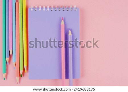 Lilac notebook, sketchbook, colored pencils in delicate tones on a pink background.Products for creativity, schoolchildren, students, teachers.Sale of office supplies for the academic year.Copyspace Royalty-Free Stock Photo #2419683175