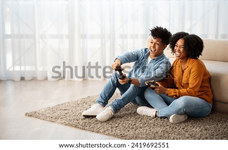Cheerful young african american woman and man gamers play at computer game with joystick, have fun, enjoy free time, in living room interior. Relationship, entertainment at home
