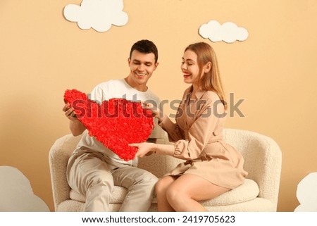 Young couple with heart sitting on sofa in clouds near beige wall