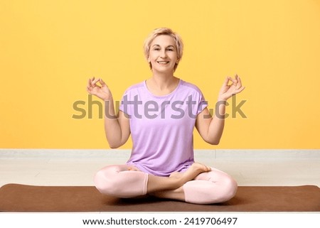 Portrait of meditating mature woman sitting on floor against yellow wall