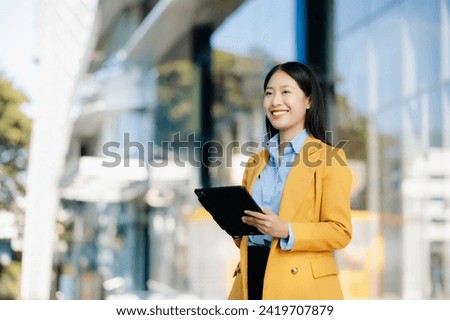 Young Asian business woman leader entrepreneur, professional manager holding digital tablet computer uon the street in big city on business center background.