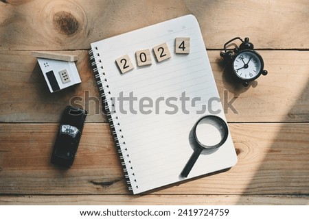 close up notebook, 2024 wooden text block, wood house, toy car, alarm clock and magnifying glass on table, to do list and mission goal wallpaper background concept