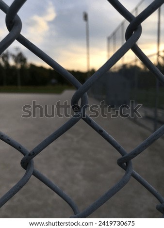 A chainlink fence with a baseball diamond in the background. Royalty-Free Stock Photo #2419730675