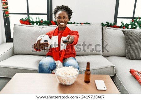 African american woman supporting soccer team sitting on sofa at home