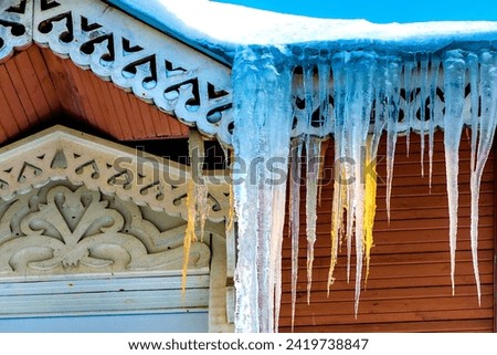 Icicles in winter and spring in a selective focus. Roof of the house is covered with snow and ice. Icicles hang from the roof, melting on a bright sunny day. Danger, the falling icicles. Thaw.