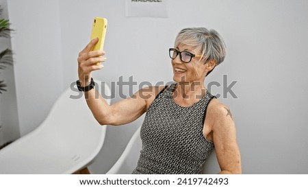 Mature woman with glasses and grey hair taking a selfie indoors