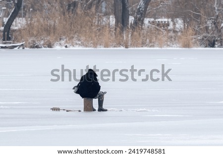 A fisherman sits on the surface of an ice-covered river and fishes in the hole