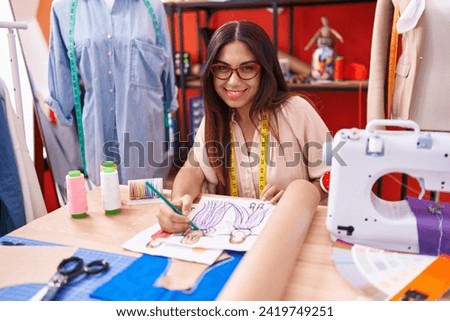 Young beautiful arab woman tailor drawing clothing design on notebook at atelier