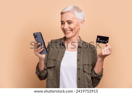 Photo of cheerful rich business woman do love shopping stay home with credit card and smartphone isolated on beige color background