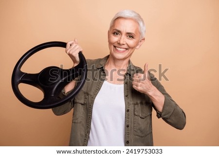Portrait of successful and experienced taxi driver female hold steering wheel thumb up recommended car service over beige color background