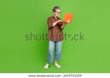 Full size photo of intelligent cheerful person wear stylish shirt look at laptop write post in blog isolated on green color background