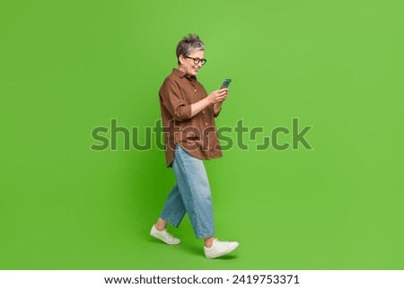 Full size photo of clever person wear stylish shirt read notification on smartphone go empty space isolated on green color background