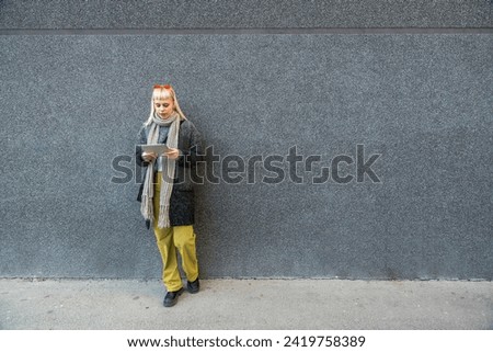 Happy hippie girl browsing a tablet working freelance and leaning on a wall of office building in the street. Hipster woman online work while waiting colleagues for staff meeting Royalty-Free Stock Photo #2419758389