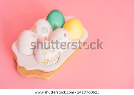 Easter eggs of different colors and in stickers in a white tray on a pink background.