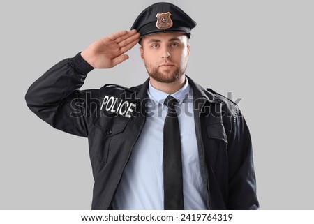 Male police officer saluting on grey background