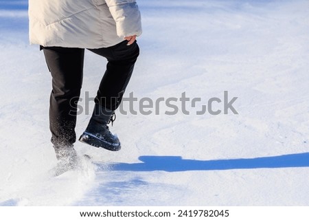 Woman's legs in winter boots walking in the snow. Background with selective focus and copy space for text