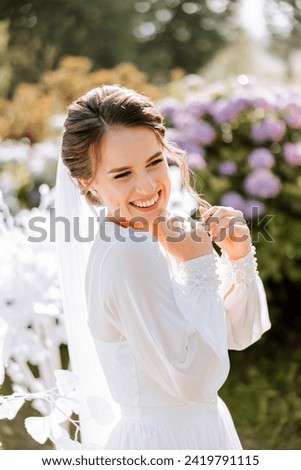 A beautiful brunette bride in an elegant robe is walking in a park with green grass and pink hydrangea flowers. Morning, meetings, wedding portrait of a cute girl. Photography and concept. Summer.