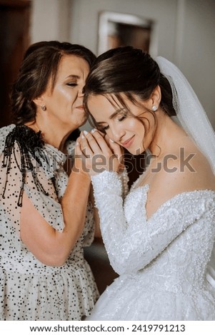 A beautiful and happy mother and her daughter, the bride, are standing next to each other. The best day for parents. Tender moments at the wedding. Royalty-Free Stock Photo #2419791213