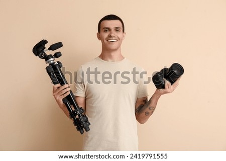 Male photographer with modern camera and tripod on beige background