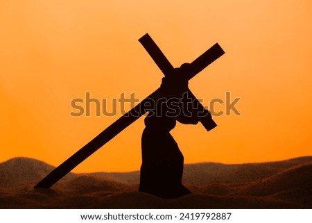 Jesus carrying wooden cross on sand against orange background. Good Friday concept Royalty-Free Stock Photo #2419792887