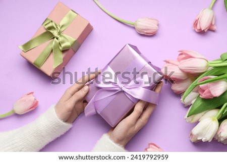 Female hands with gift boxes and beautiful tulips on purple background. International Women's Day