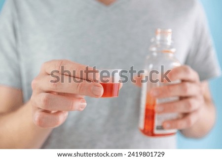 Man drinking dose of liquid medicine syrup for treatment cold and flu in measuring cup. Male taking liquid drug from meds bottle. Taking medicine, health care, pharmacy concept Royalty-Free Stock Photo #2419801729