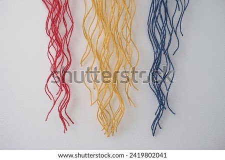 Suspended against a white backdrop, the cotton fringed ends in Romanian flag colors-red, yellow, and blue- form a flame shape striking composition.