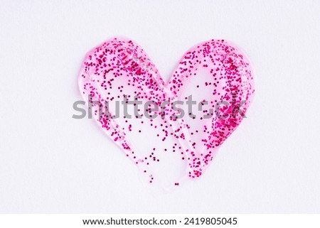 Pink shimmering lip gloss texture in heart shape, texture stroke isolated on white background. Cosmetic product swatch. Glittering sample Royalty-Free Stock Photo #2419805045