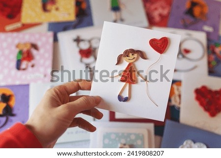 Hand holding quilling card with stick figure girl with heart balloon. woman making greeting cards. Hand made of paper quilling technique. Handicraft at home. Hobby, home office.