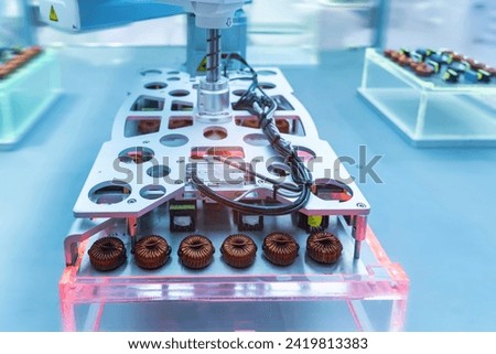 artificial intelligence machine at industrial manufacture factory for toroidal coils with magnetic ferrite core wrapped in copper wire on electronic components pile Royalty-Free Stock Photo #2419813383