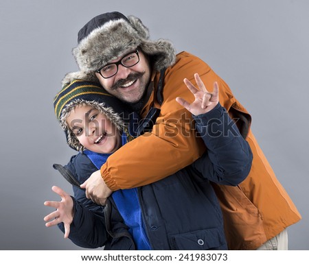 Portrait of happy father and son of ten years wearing winter clothes over gray background.